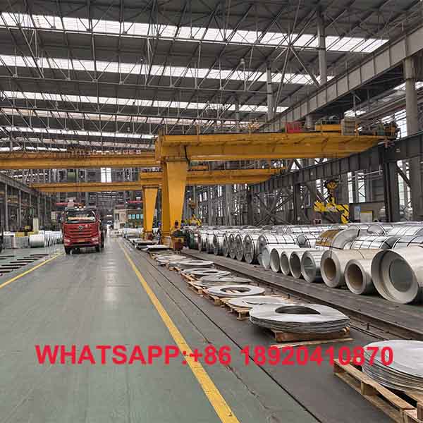 Lorong tengah gudang penyimpanan masif material logam gulungan berkilau untuk kepastian ketersediaan harga coil baja ringan.